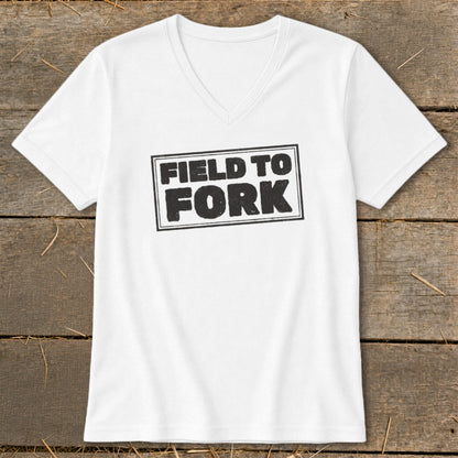 A white V-neck t-shirt rests on a rustic wooden background, featuring the words Field to Fork printed in black inside a box.