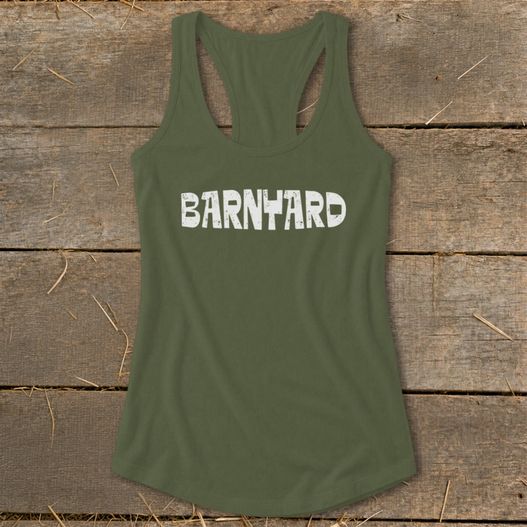 An olive green racerback tank top featuring the distressed white text "BARNYARD" across the chest, laid flat on a rustic wooden background.