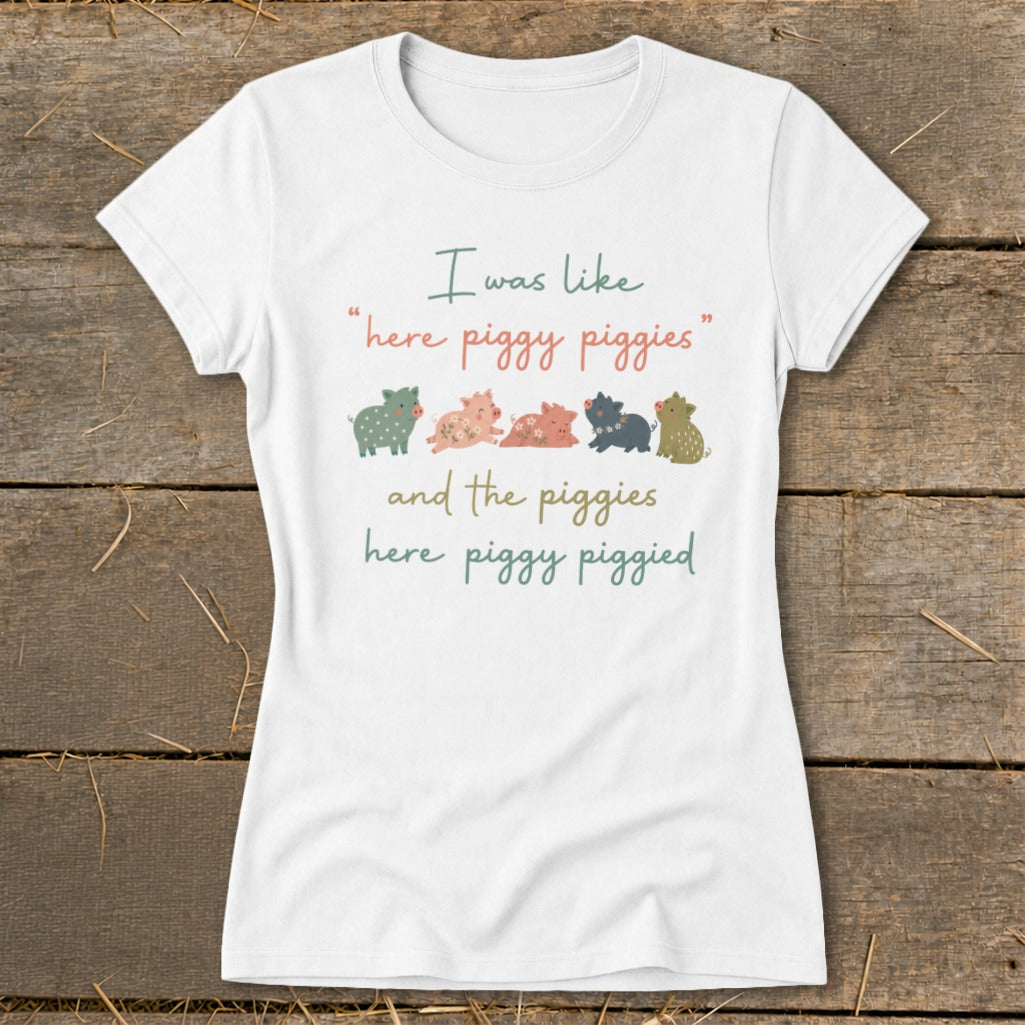 White t-shirt with text "I was like 'here piggy piggies' and the piggies here piggy piggied" and five cartoon pigs.