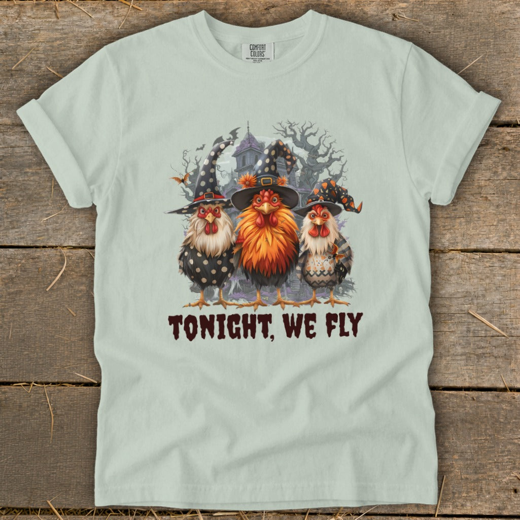 Three chickens in witch hats stand before a spooky house with bats.