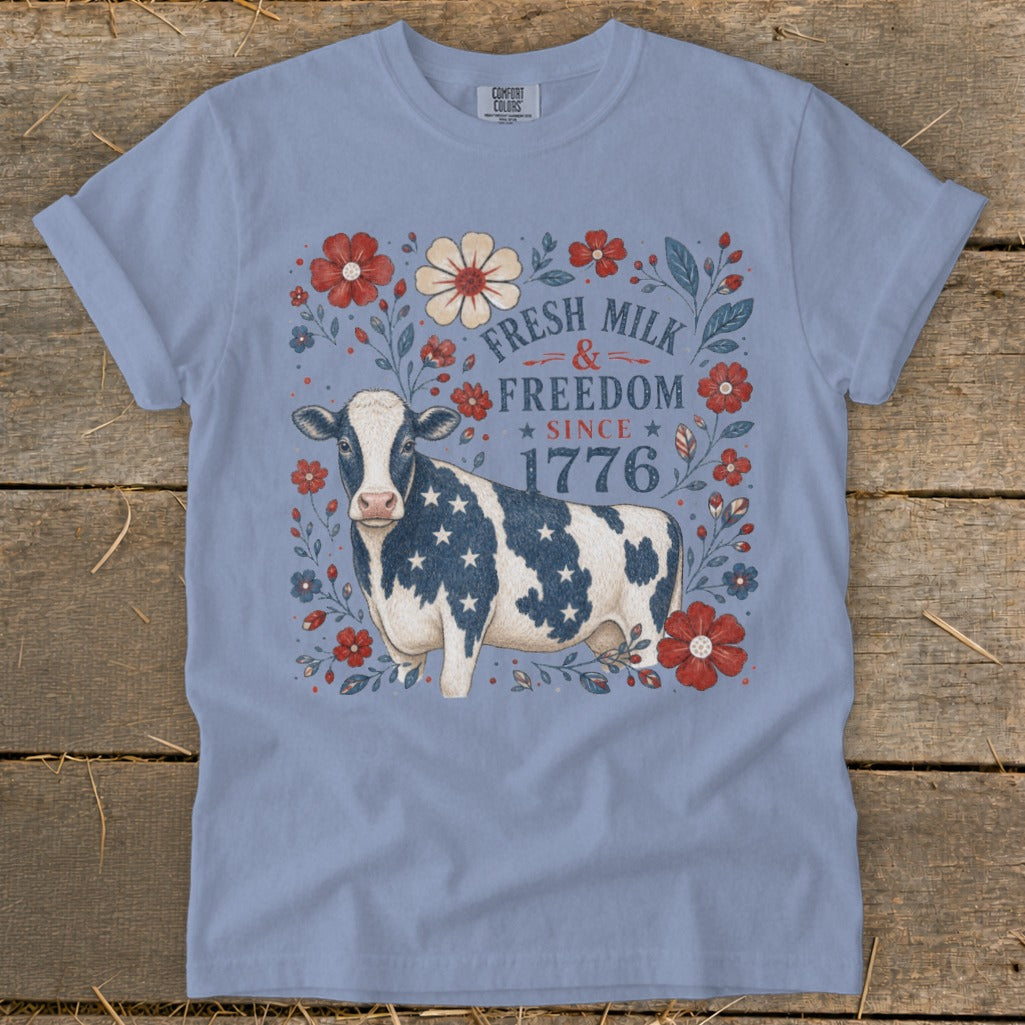 Blue t-shirt with a cow, red flowers, and text "Fresh Milk & Freedom Since 1776".