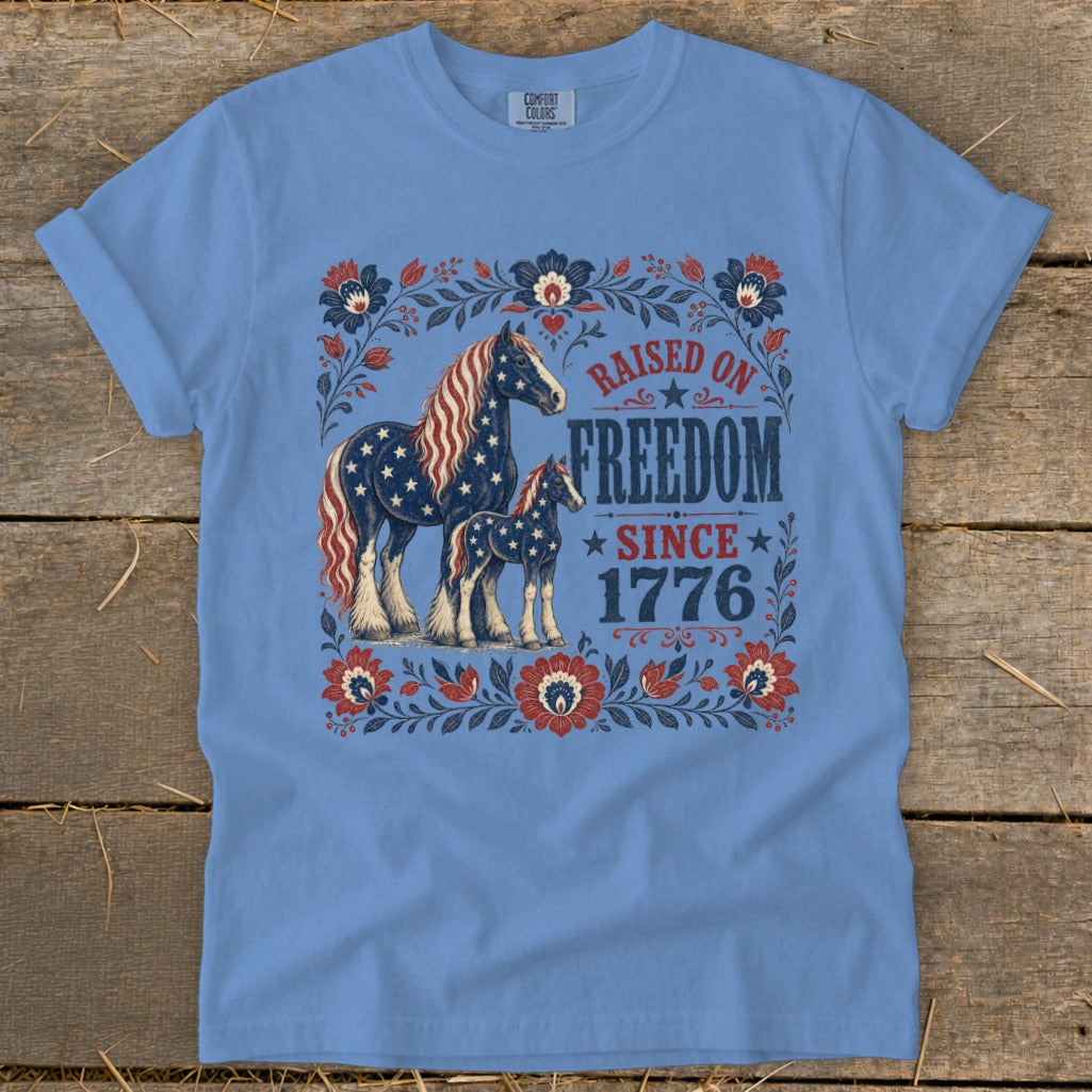 T-shirt with vintage horses and floral border, reading "Raised on Freedom Since 1776".