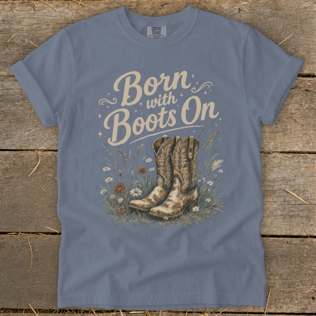 Blue t-shirt with "Born with Boots On" text over cowboy boots and flowers.