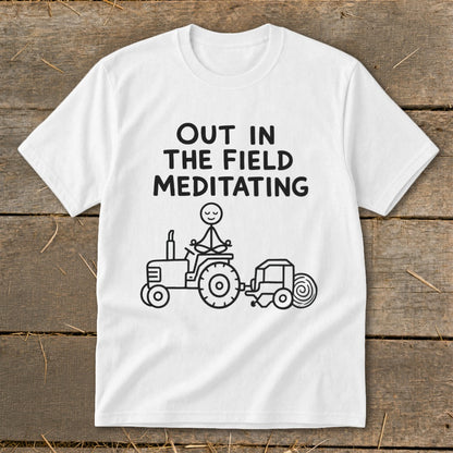 White t-shirt with text "OUT IN THE FIELD MEDITATING" and a stick figure meditating on a tractor.