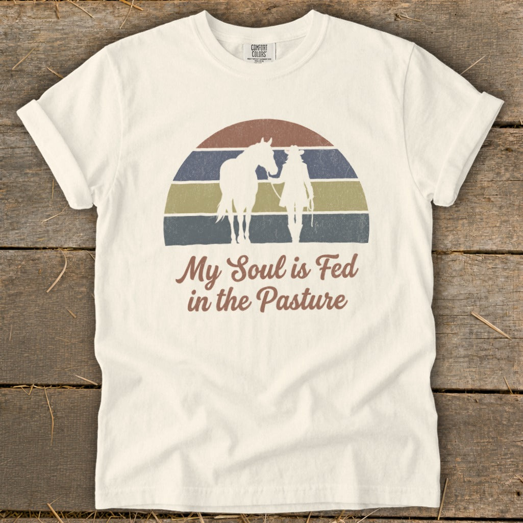 White t-shirt with vintage sunset graphic of horse and rider, "My Soul is Fed in the Pasture."