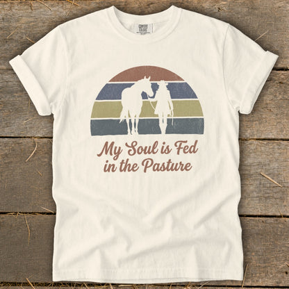 White t-shirt with vintage sunset graphic of horse and rider, "My Soul is Fed in the Pasture."