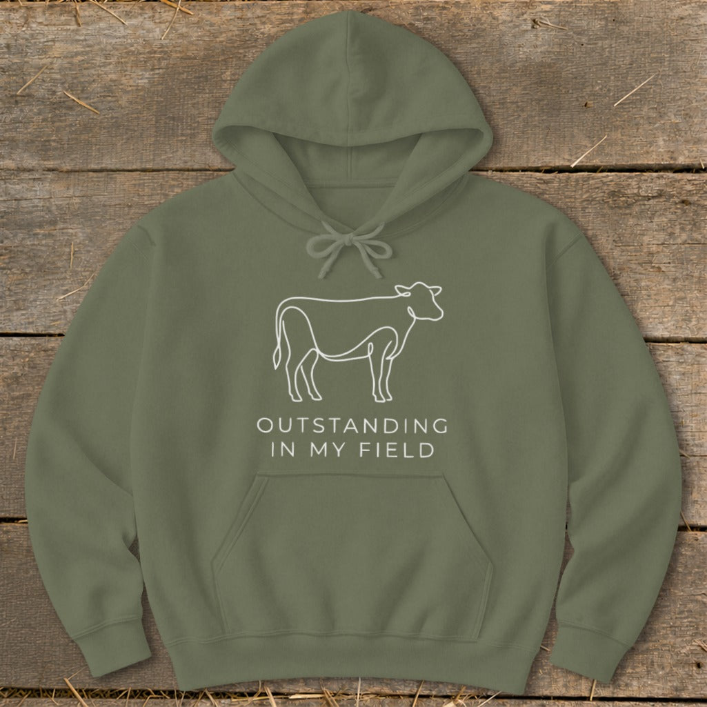 Olive green hoodie with white line art cow and text "OUTSTANDING IN MY FIELD".