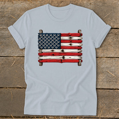 Light blue t-shirt featuring a graphic of the American flag made of painted wooden planks and horseshoes, laid on a rustic wooden background.