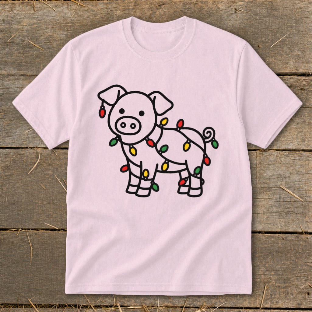 A light pink t-shirt featuring a cartoon pig wrapped in colorful Christmas lights, displayed on wood.