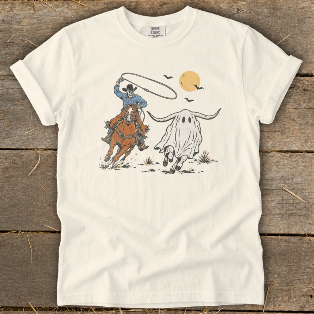 Skeleton cowboy on horse lassoing a ghost longhorn with bats and sun in background.